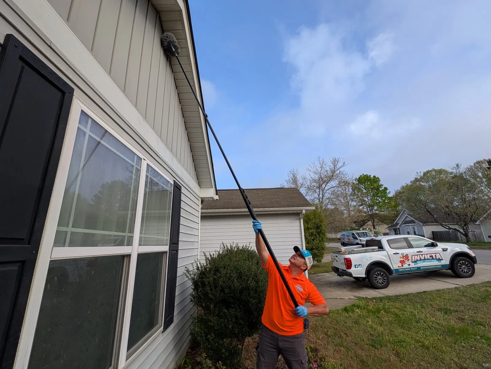 Invicta technician brushing webs from a home’s eaves with an extension pole