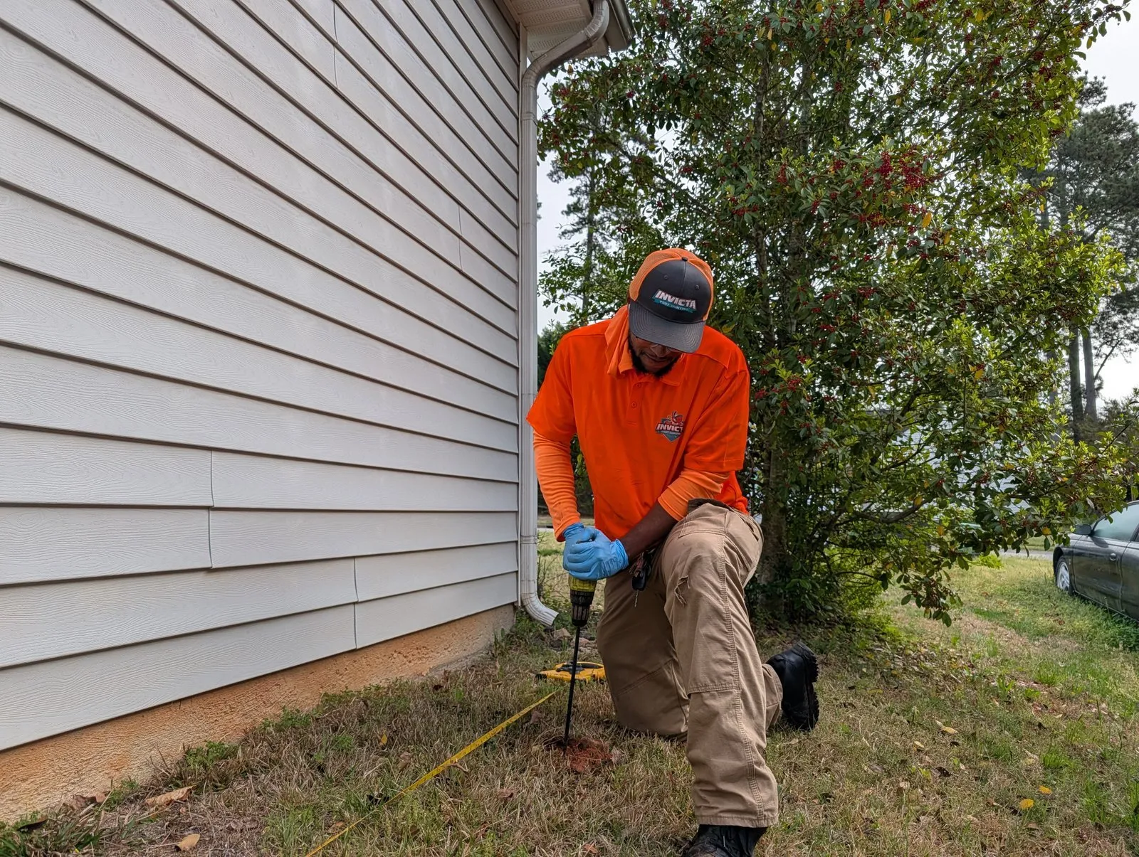 Invicta technician treating beside a shrub along a home’s siding