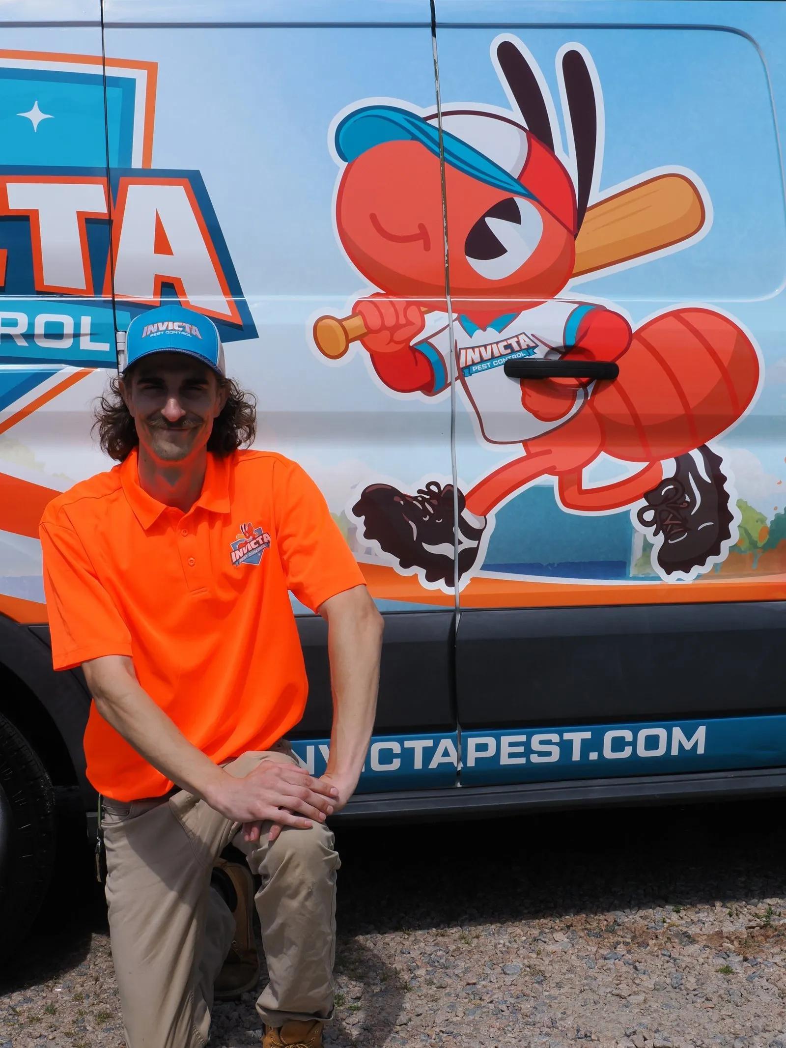Invicta technician kneeling in front of the ant mascot on an Invicta van