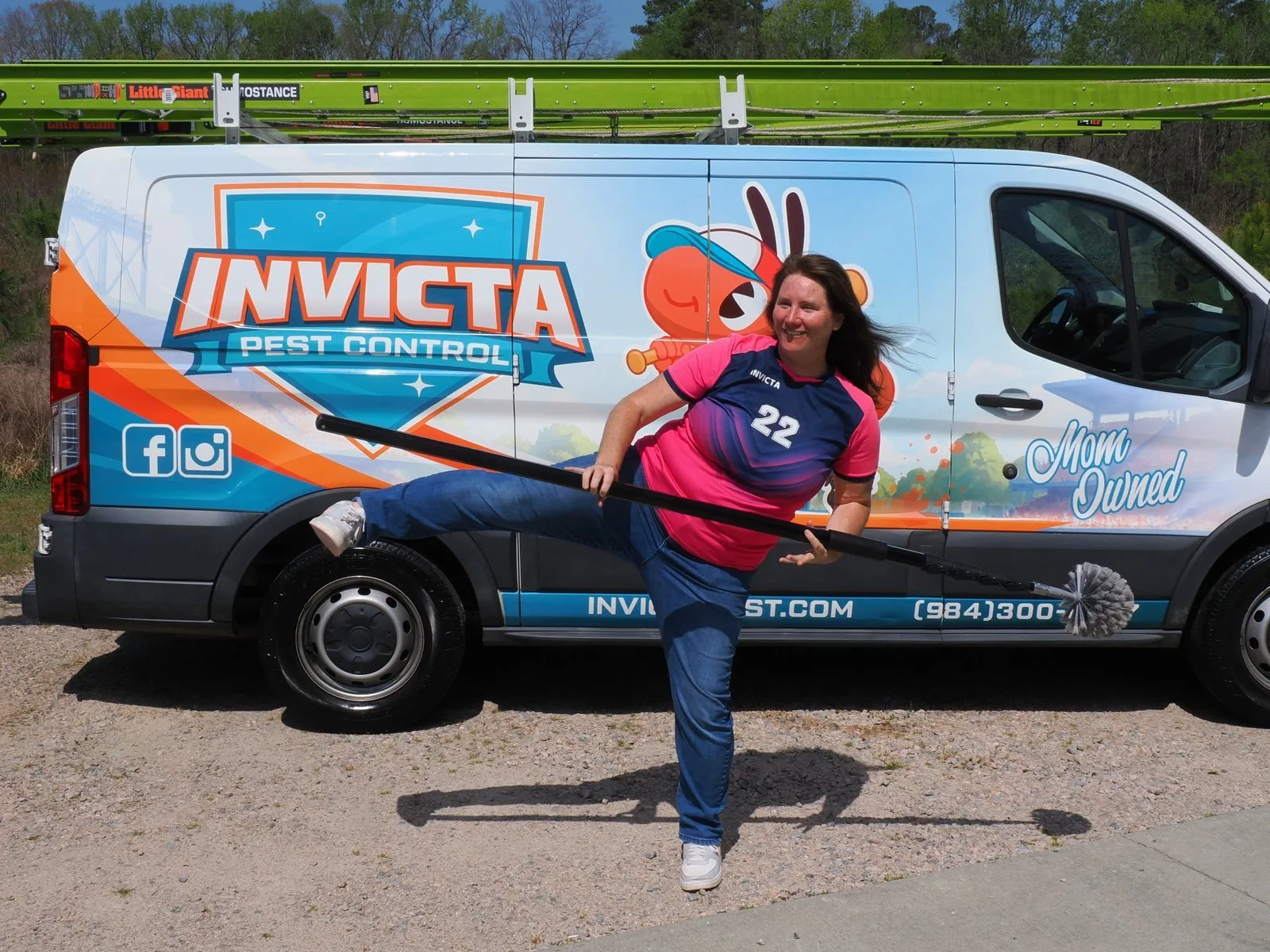 Elizabeth Gilbert kicking up a heel with a web brush in front of an Invicta van