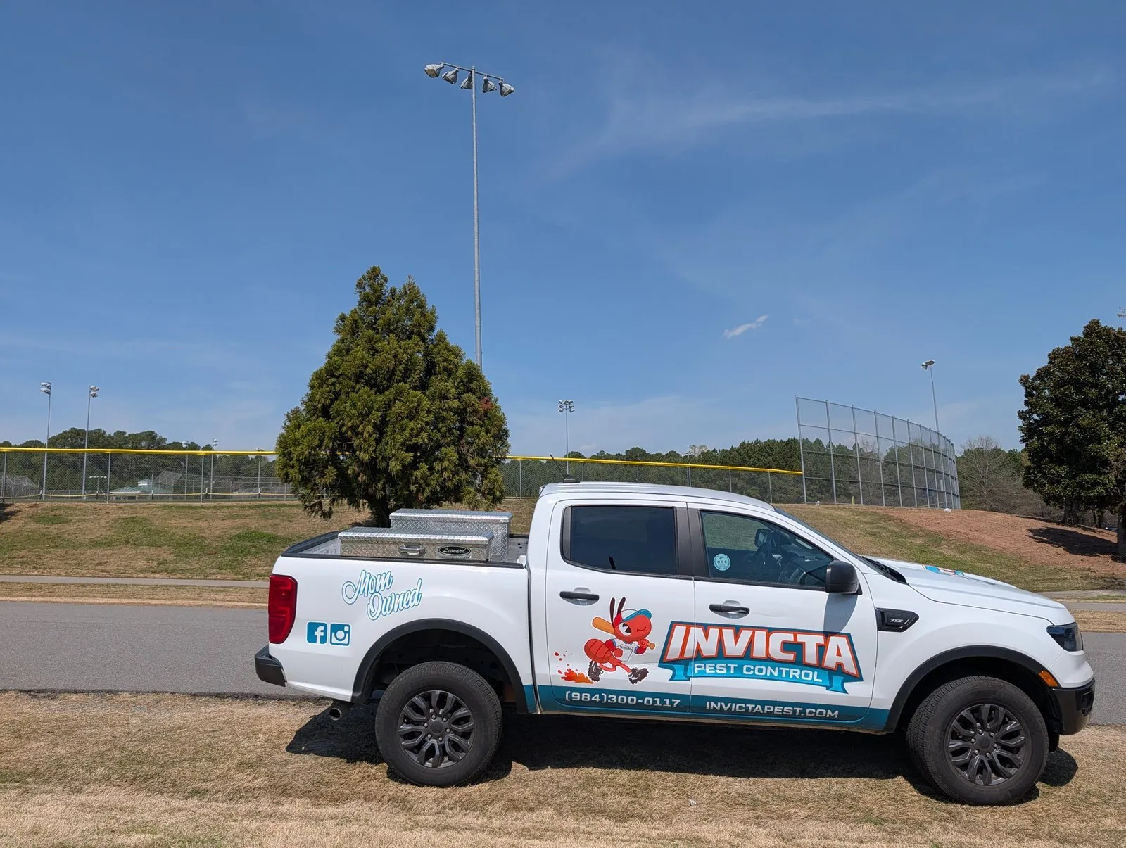 Invicta Pest Control truck parked beside a ballfield